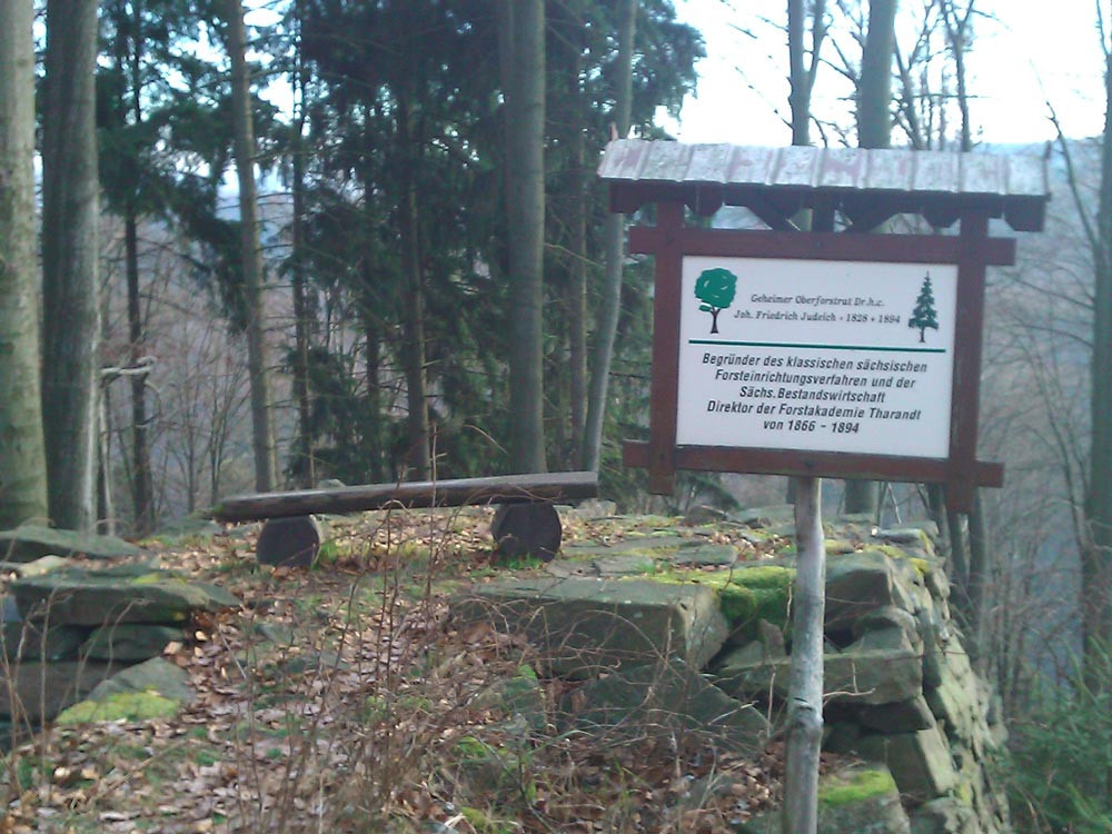 Schild im Wald vor einer Bank